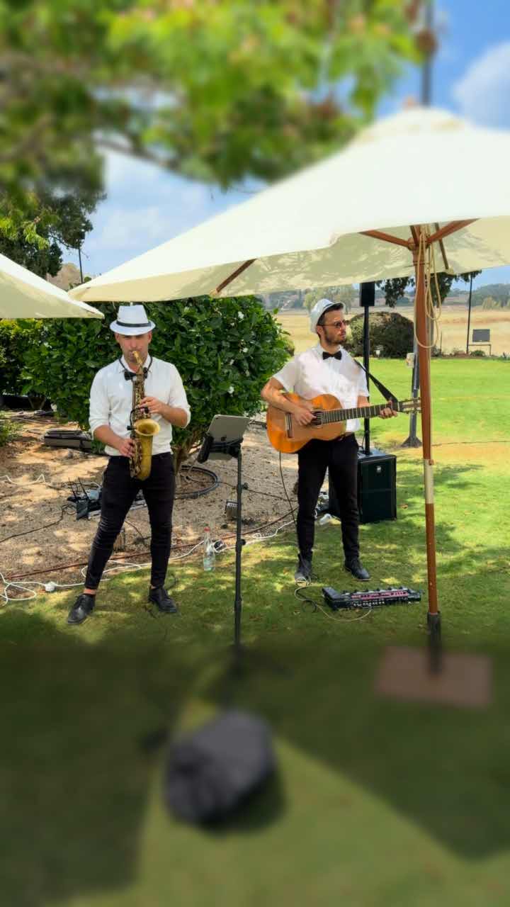 הרכב לקבלת פנים – טריו Jazzmen: סקסופוניסט וגיטריסט מנגנים מתחת לשמשיות לבנות בקבלת פנים של חתונה בגן