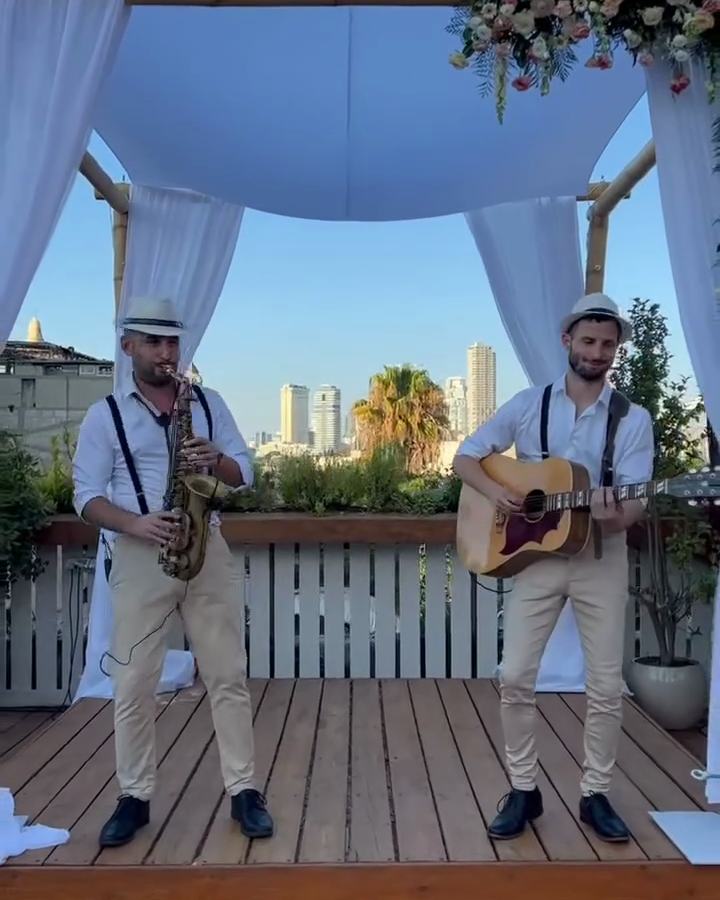 הרכב לקבלת פנים לטינוס – סקסופון וגיטרה מנגנים מתחת לחופה על גג ביפו מול קו הרקיע של תל אביב