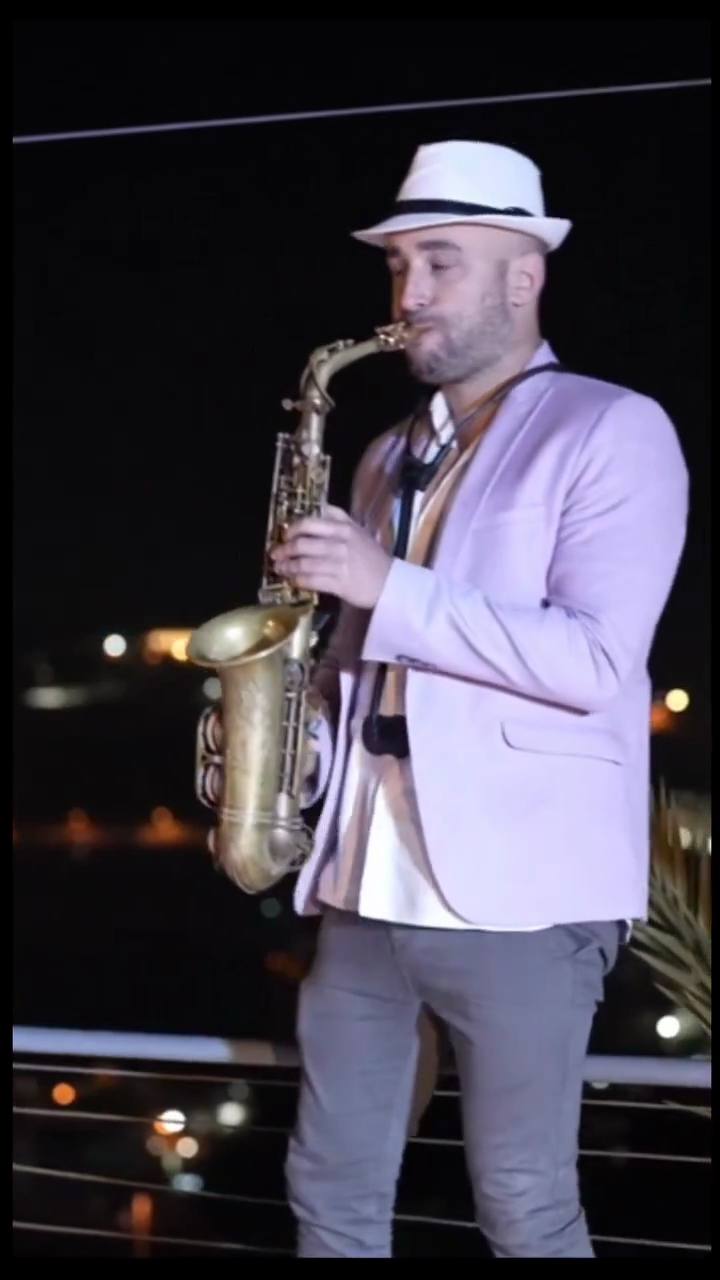 מורה לסקסופון במודיעין – טל רודובסקי מנגן בסקסופון אלט על גג בערב, אורות העיר מאחוריו