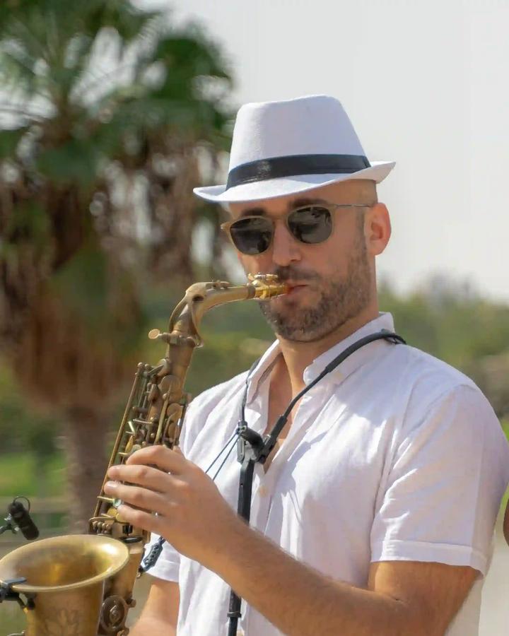 מורה לסקסופון במודיעין – טל רודובסקי מנגן בסקסופון בחוץ, עצי דקל ברקע