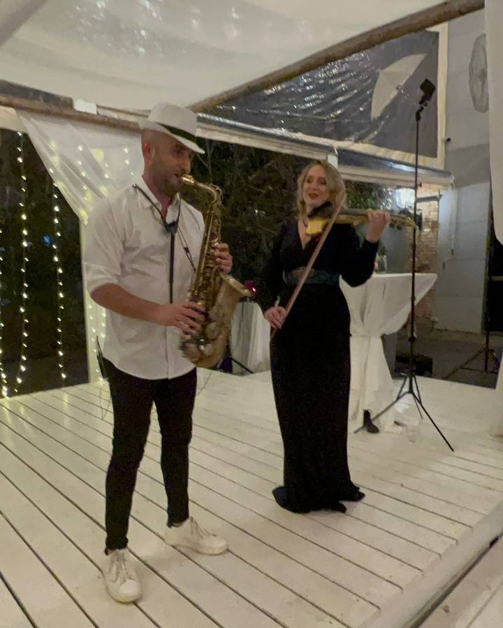 כנריות לחתונה – כנרית בשמלת ערב שחורה וסקסופוניסט מנגנים מתחת לאוהל לבן מואר